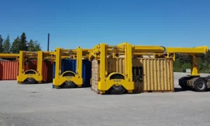 Straddle carriers levantando contenedores marítimos en una terminal logística industrial, con maquinaria pesada de carga y almacenamiento de contenedores en puerto seco